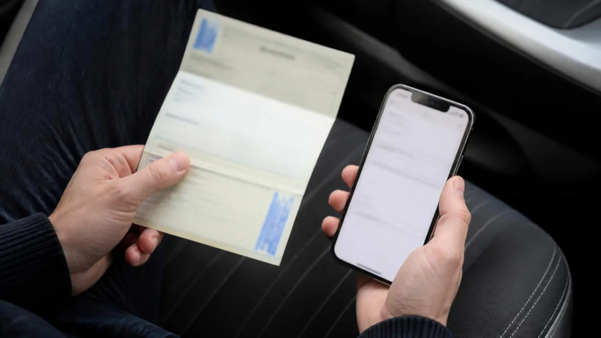 Mani che tengono la carta di circolazione accanto a uno smartphone per verificare il telaio