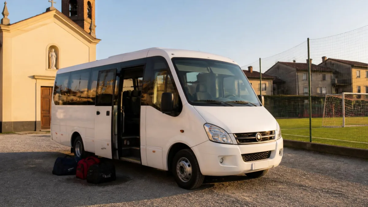 patente-d1-cosa-si-guida-cover Minibus bianco parcheggiato nel cortile di un oratorio accanto a un campo da calcio, con borse sportive vicino alla porta