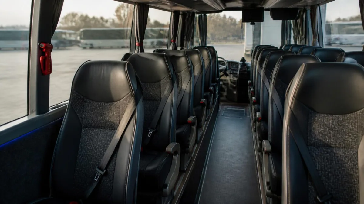Interno di un pullman vuoto con cinture sui sedili e martelletto di emergenza accanto al finestrino
